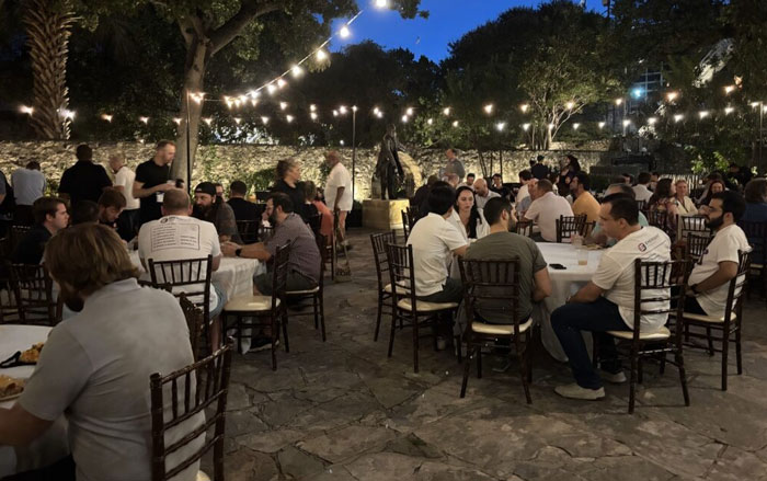 Dozens of people from the Emergent Software team are dining at a large outdoor venue. 
