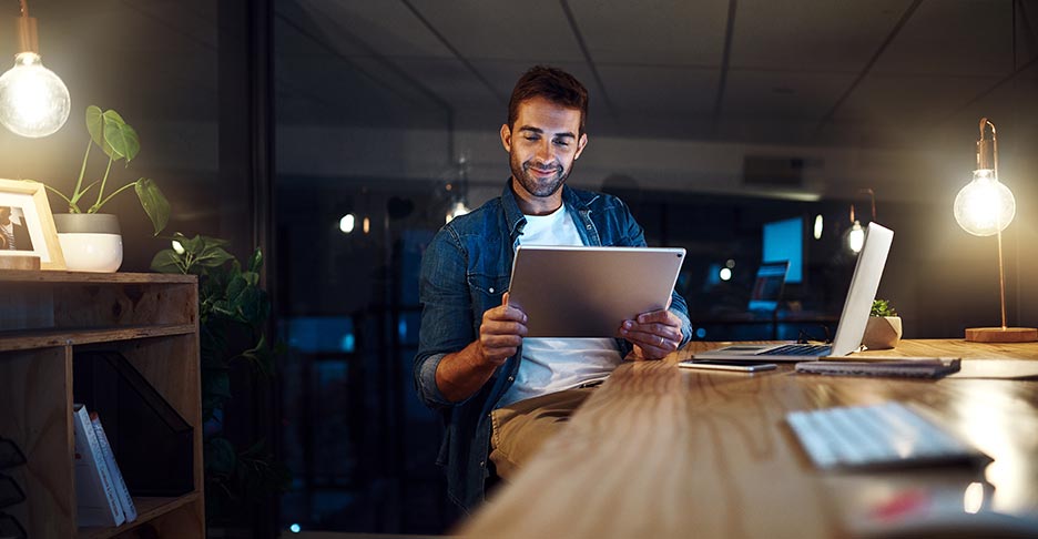 Business professional sitting in an office at night. They are reviewing information on their tablet.