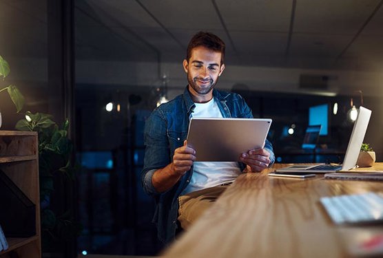 Business professional sitting in an office at night. They are reviewing information on their tablet.