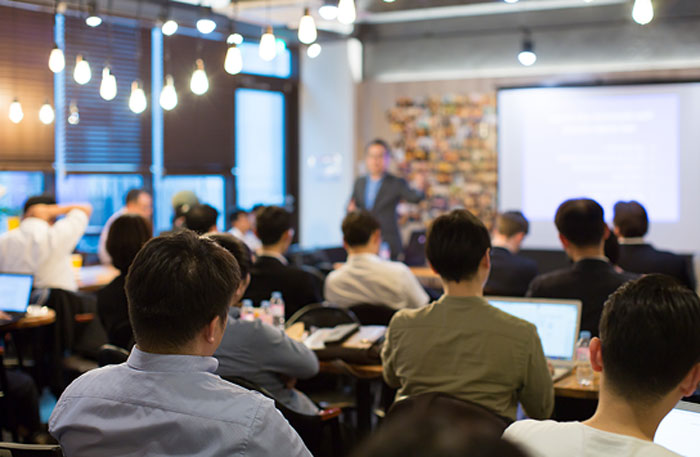 Person is lecturing a room full of business professionals.